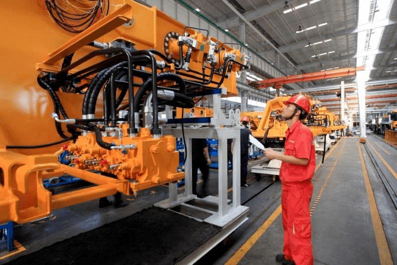 Worker beside a large orange tracked construction machine in an industrial assembly hall.