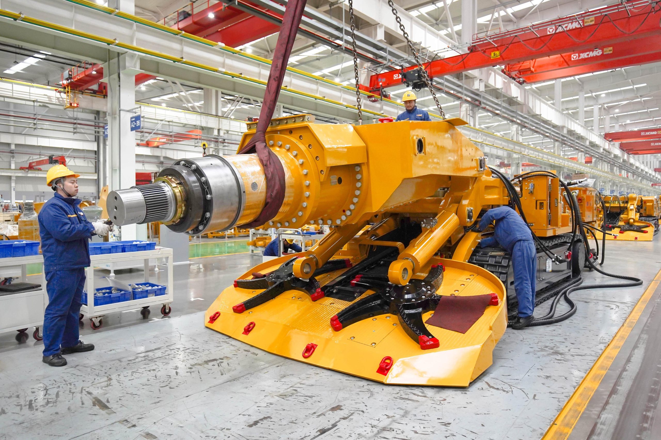 Large yellow tracked equipment with workers in an industrial assembly hall.