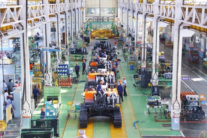 Worker examining heavy machinery components inside an industrial assembly hall.