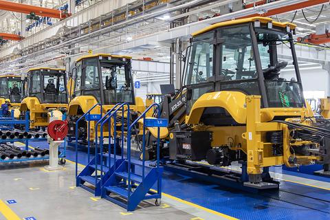 Heavy machinery assembly line with several crawler machines inside a production hall.